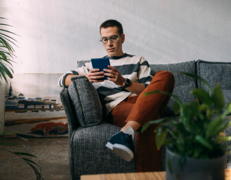 Actor portrayal of a person sitting on a couch living with hemophilia, surrounded by text explaining how hemophilia can affect daily life.