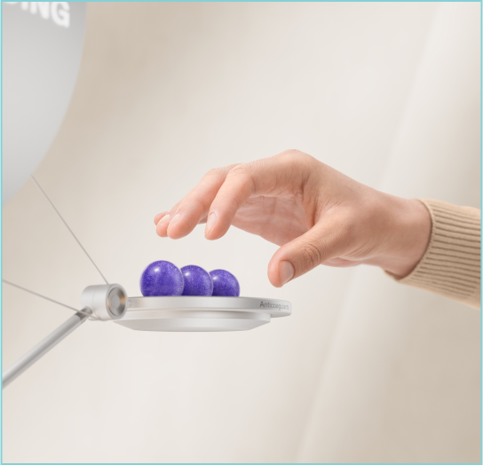 A hand hovering over a scale with three purple marbles representing procoagulants.